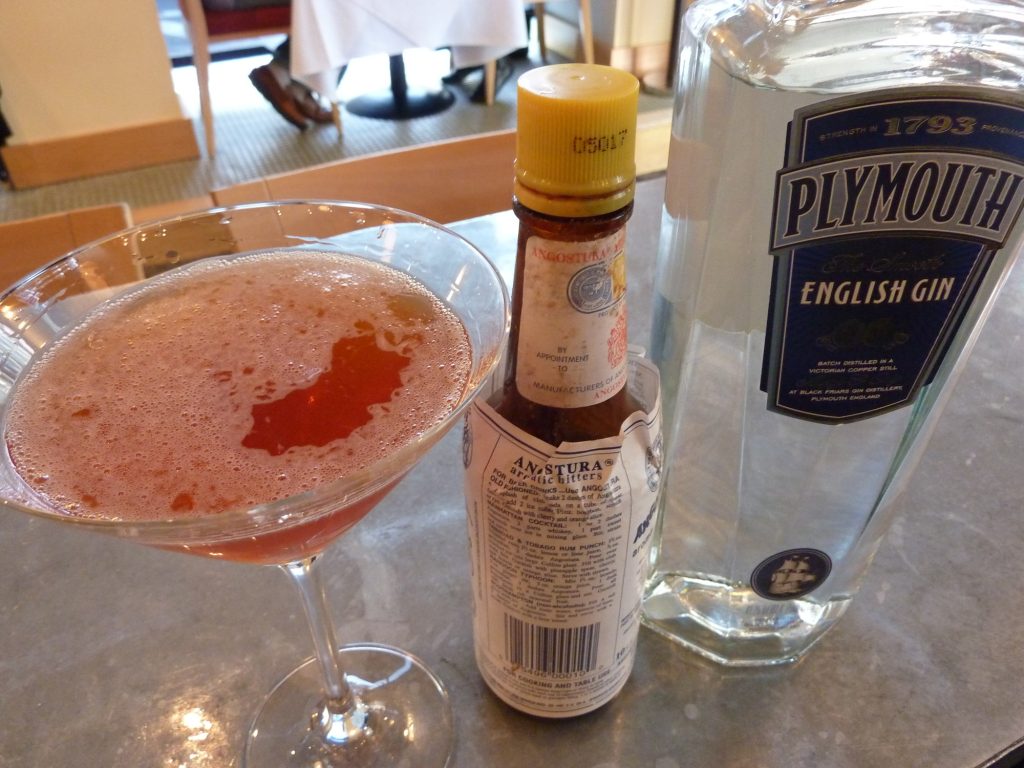 a glass of pink gin and bottles of bitters and gin