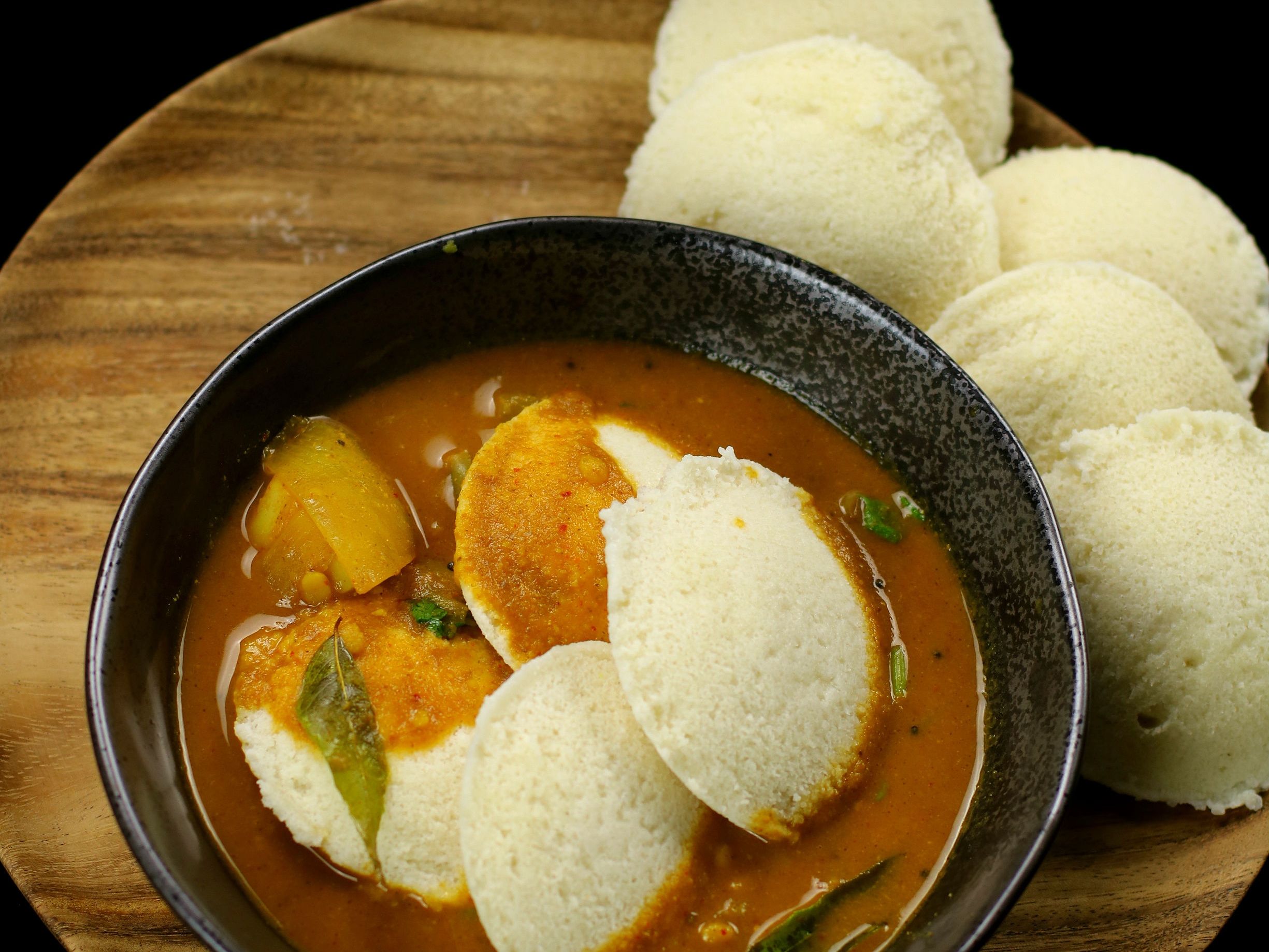 a bowl of sambar on a serving platter with idli