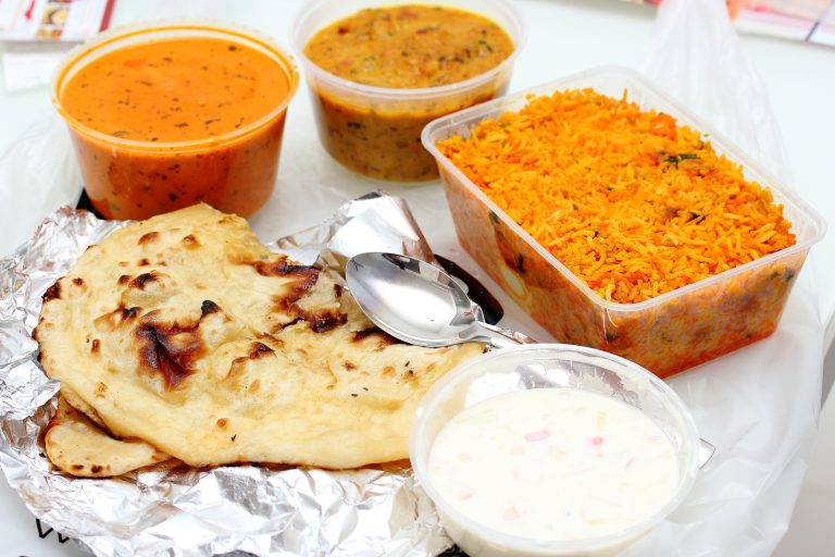 indian takeaway food in containers, with a naan in the foreground