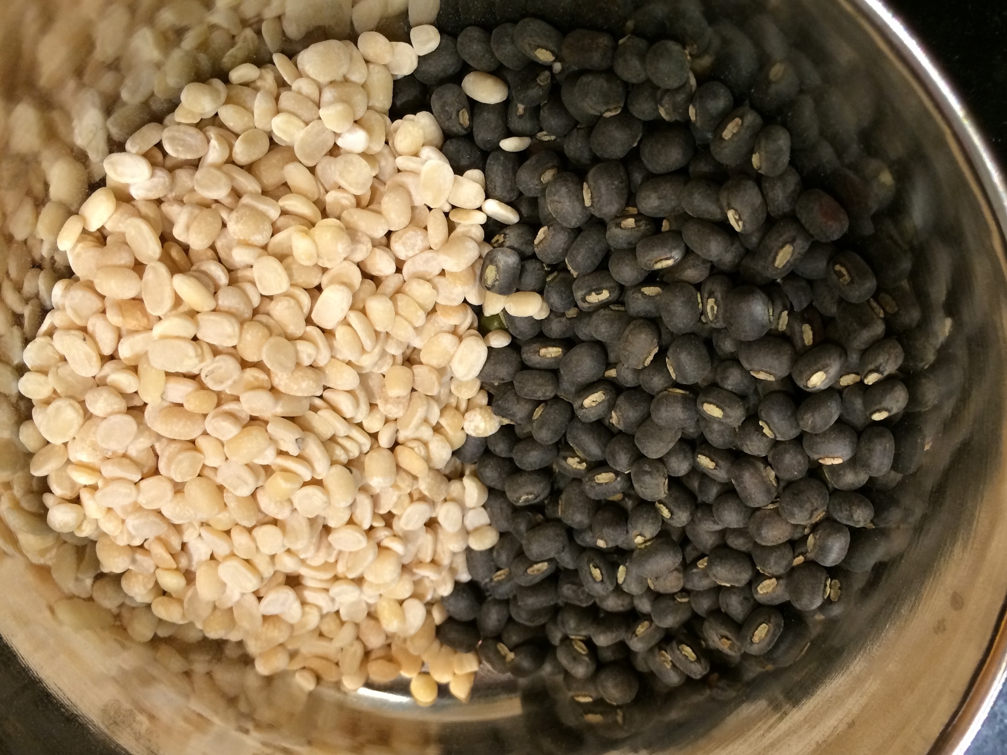 a bowl of black split lentils, half with skin on, and the other with skin removed
