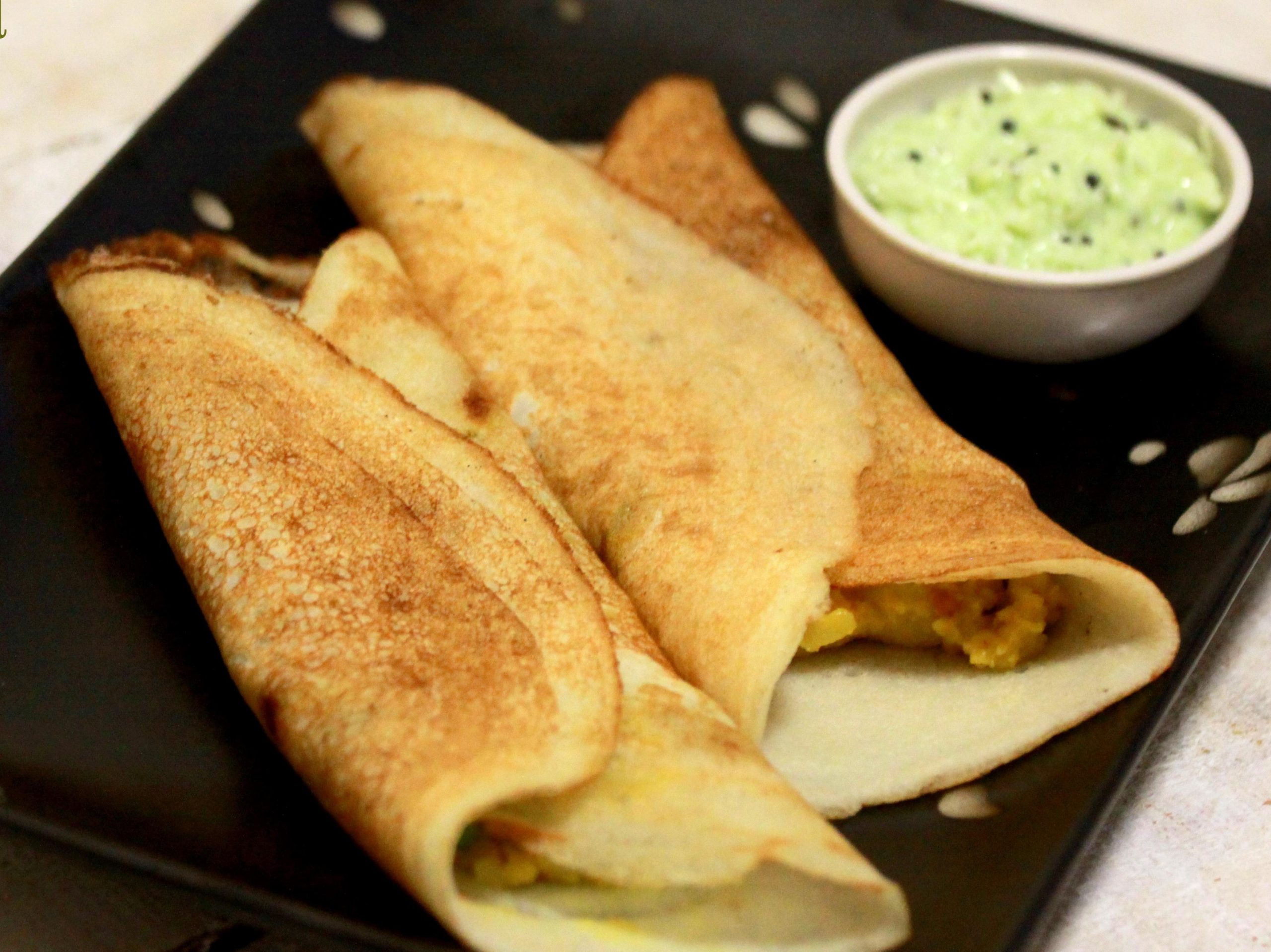 two masala dosa on a plate with serving dish of coconut chutney