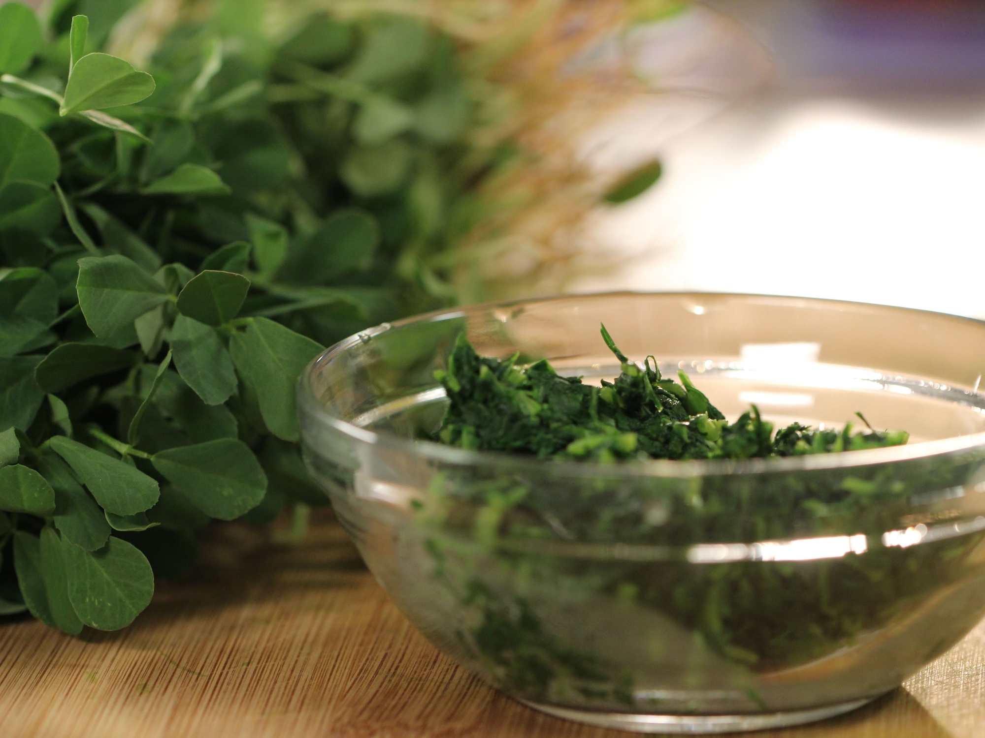 a bowl of chopped fenugreek leaves, with a fresh bunch in background