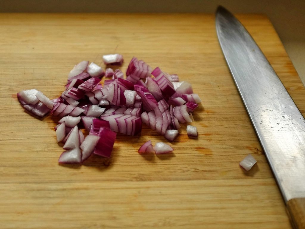 A mound of chopped onion on a chopping board with knife to right side