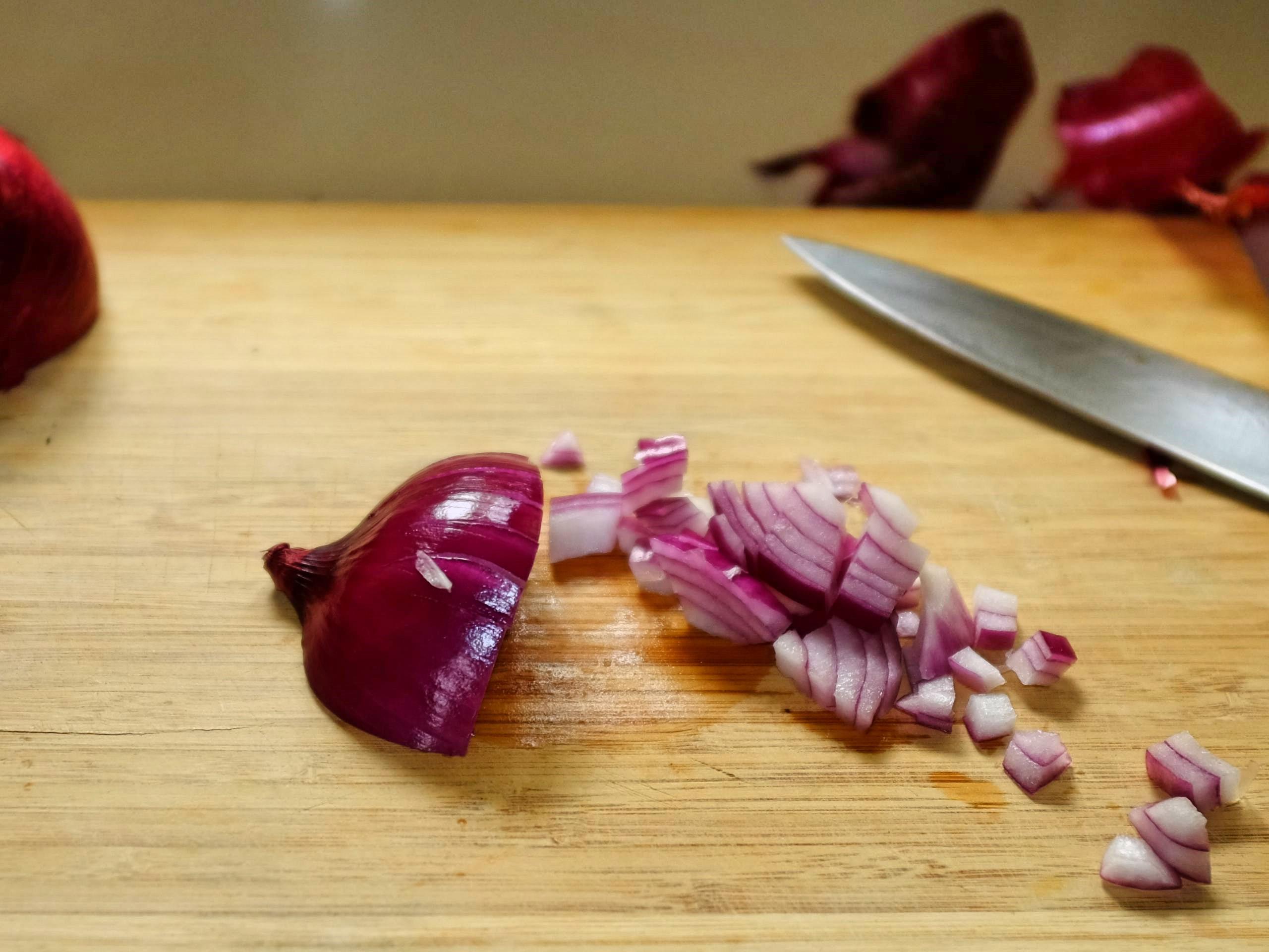 An onion on a chopping board showing second cut across the first cut