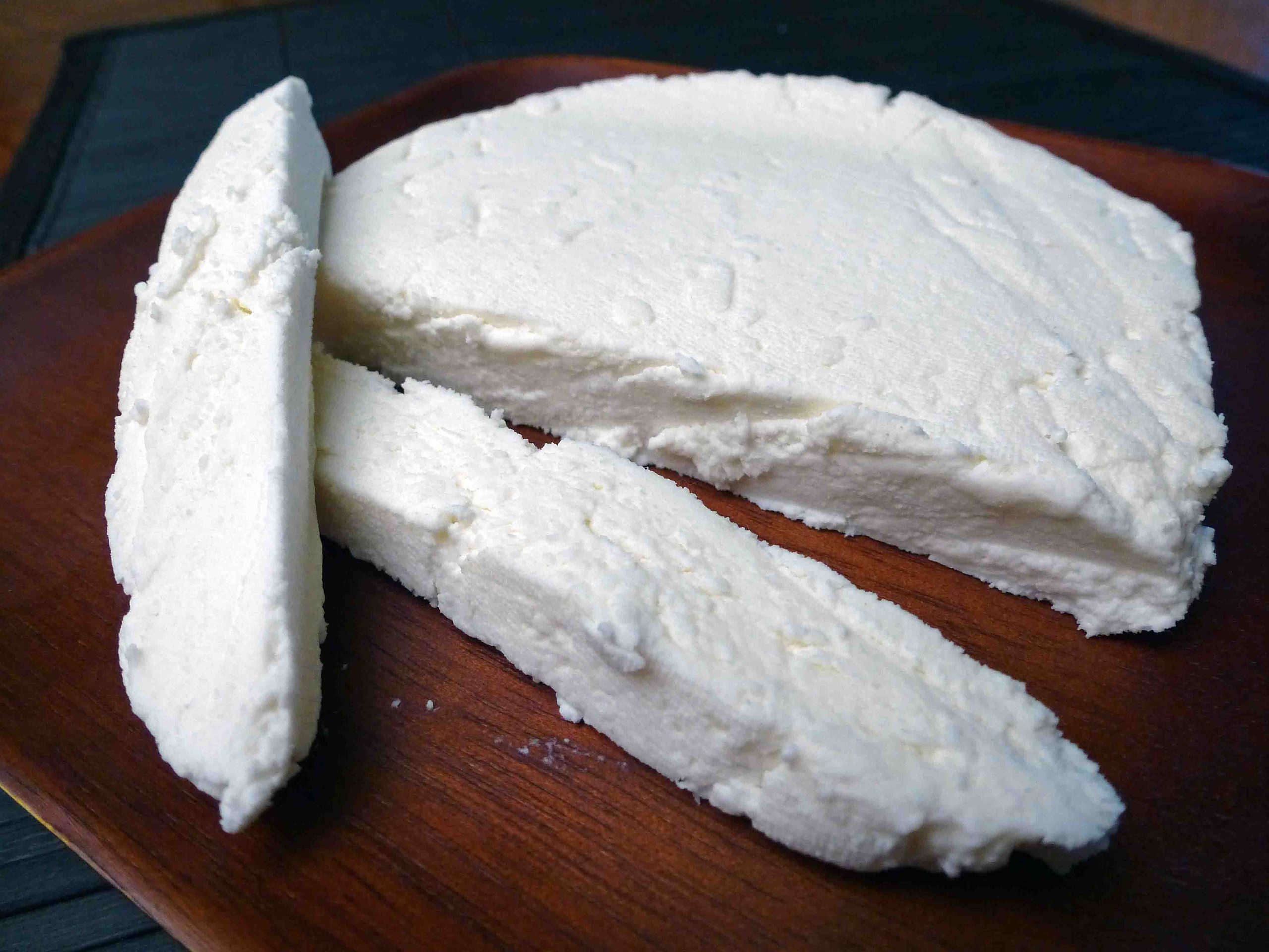 a block of paneer, partly cut, on chopping board