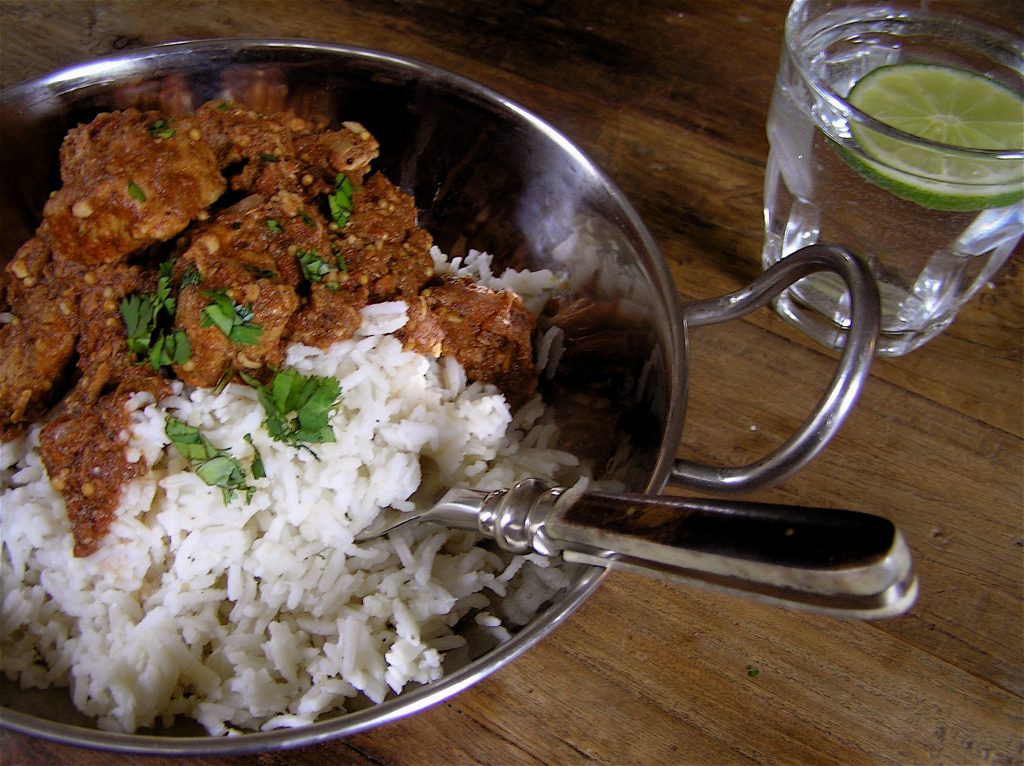 a serving of pork vindalu with rice and a glass of lime water