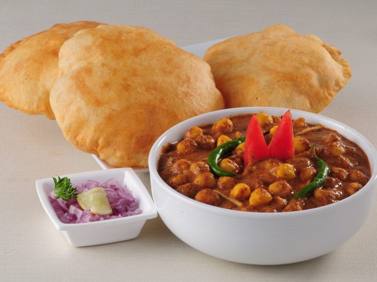 a stack of puri with a bowl of chole and an onion salad