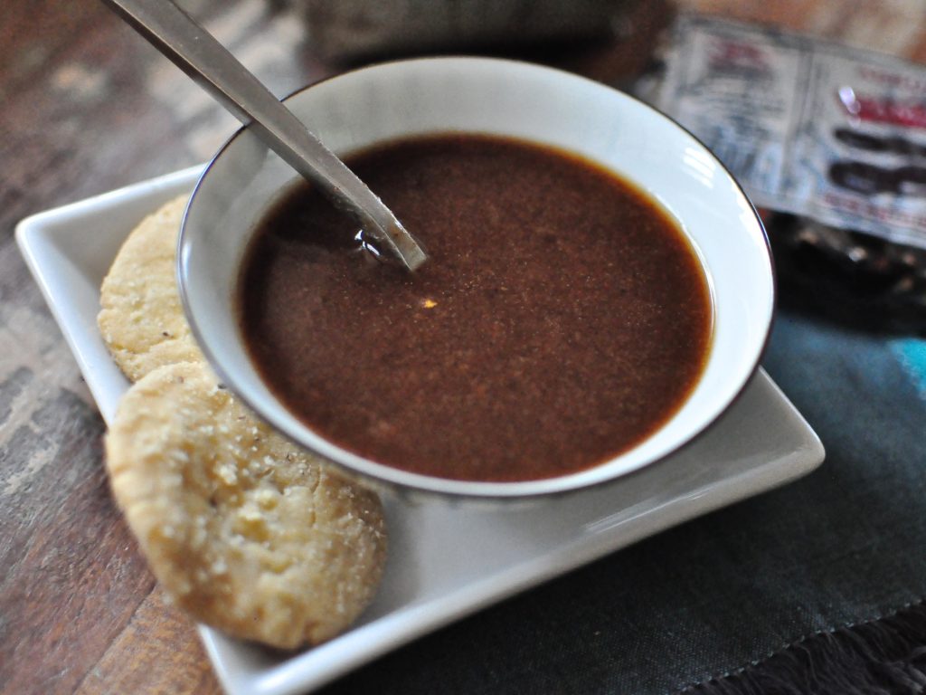 a bowl of tamarind and date chutney with some papdi on the side